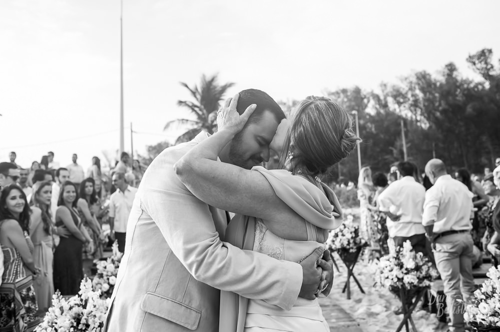 mãe do noivo beijando o noivo na testa no altar no casamento ao ar livre na praia do recreio