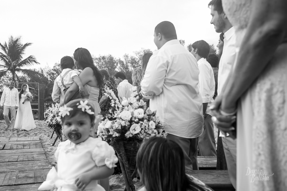 noiva entrando com o pai para a cerimonia de casamento ao ar livre na praia do recreio e daminha fofa no primeiro plano