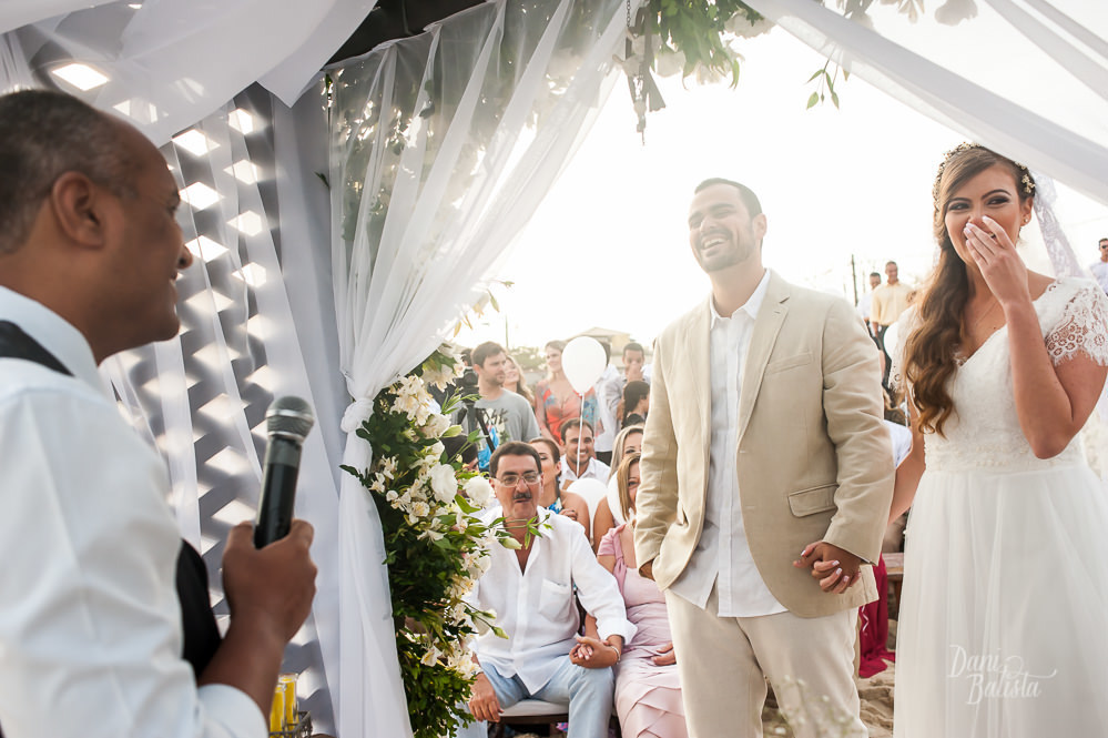 noivos rindo com o celebrante durante cerimonia diurna de casamento ao ar livre na praia do recreio