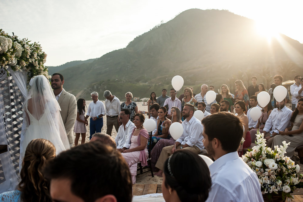 cerimonia de casamento ao ar livre no pôr-do-sol com convidados segurando balões brancos na praia do recreio