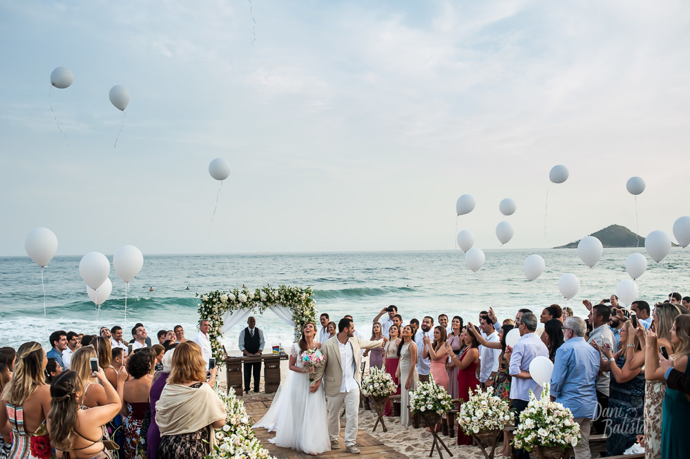 noivos saindo da cerimonia de casamento ao ar livre com balões brancos na praia do recreio