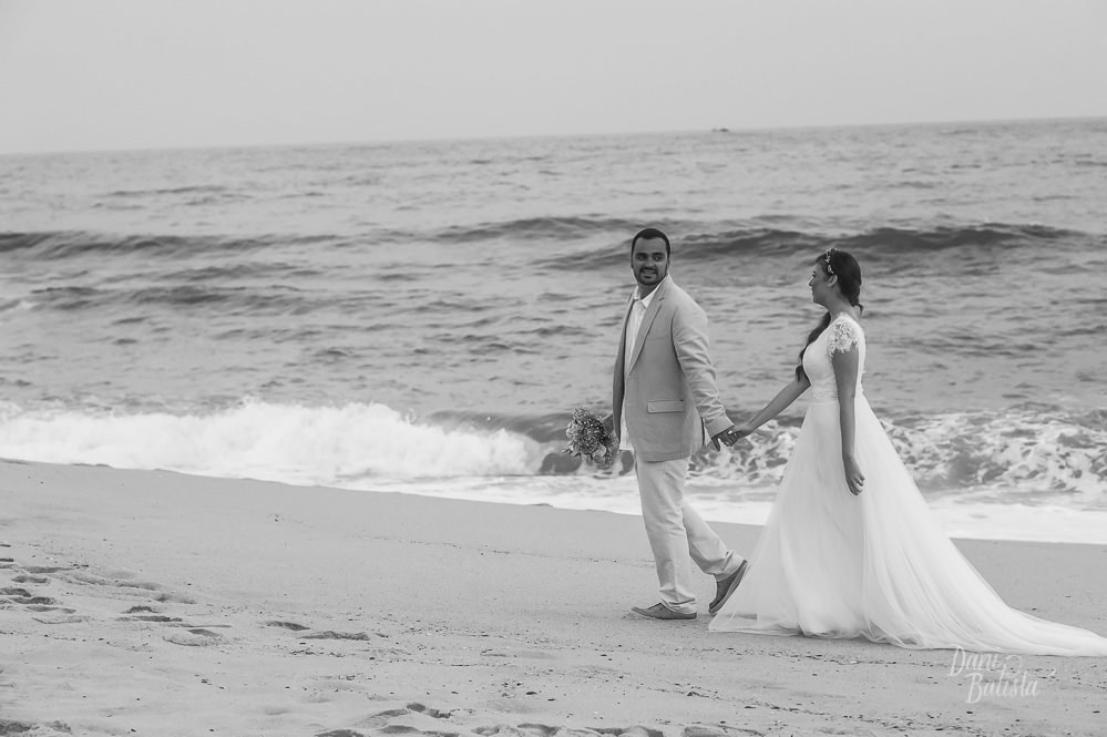 noivo segurando o bouquet  caminhando com a noiva na praia após casamento ao ar livre na praia do recreio
