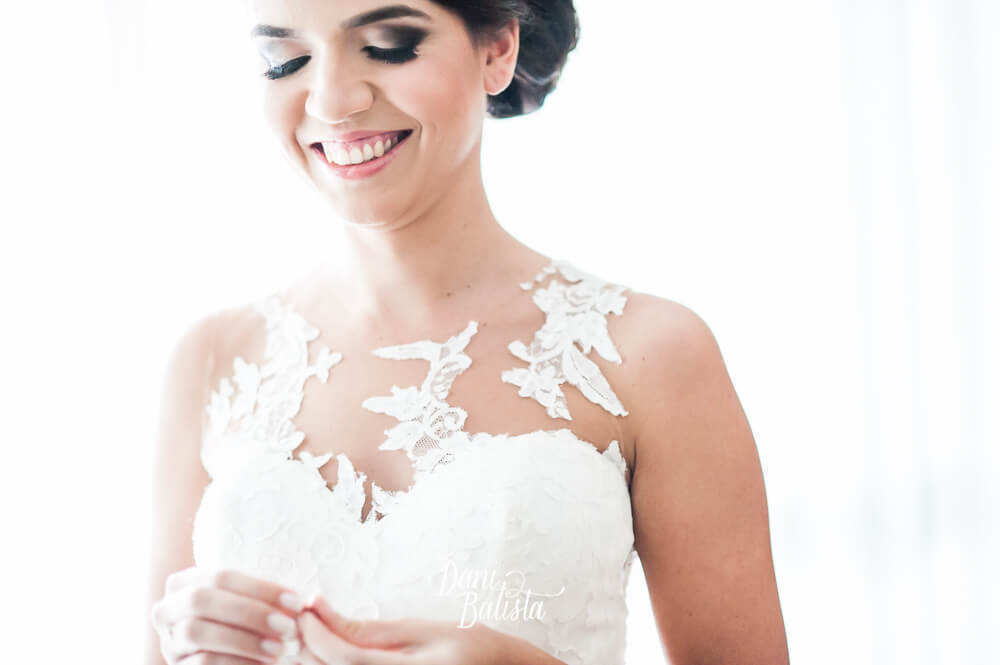 noiva colocando o brinco de pérolas com decote de renda em vestido de noiva da pronovias