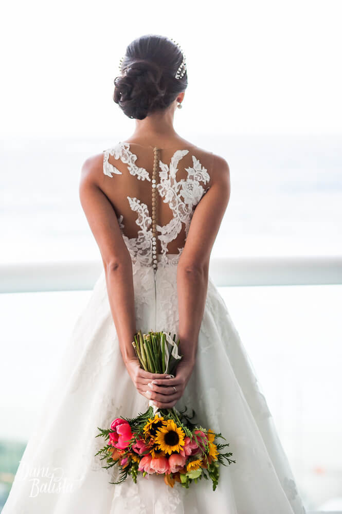 detalhe dos botões marrons no decote de renda nas costas do vestido de noiva da pronovias e bouquet de girassol