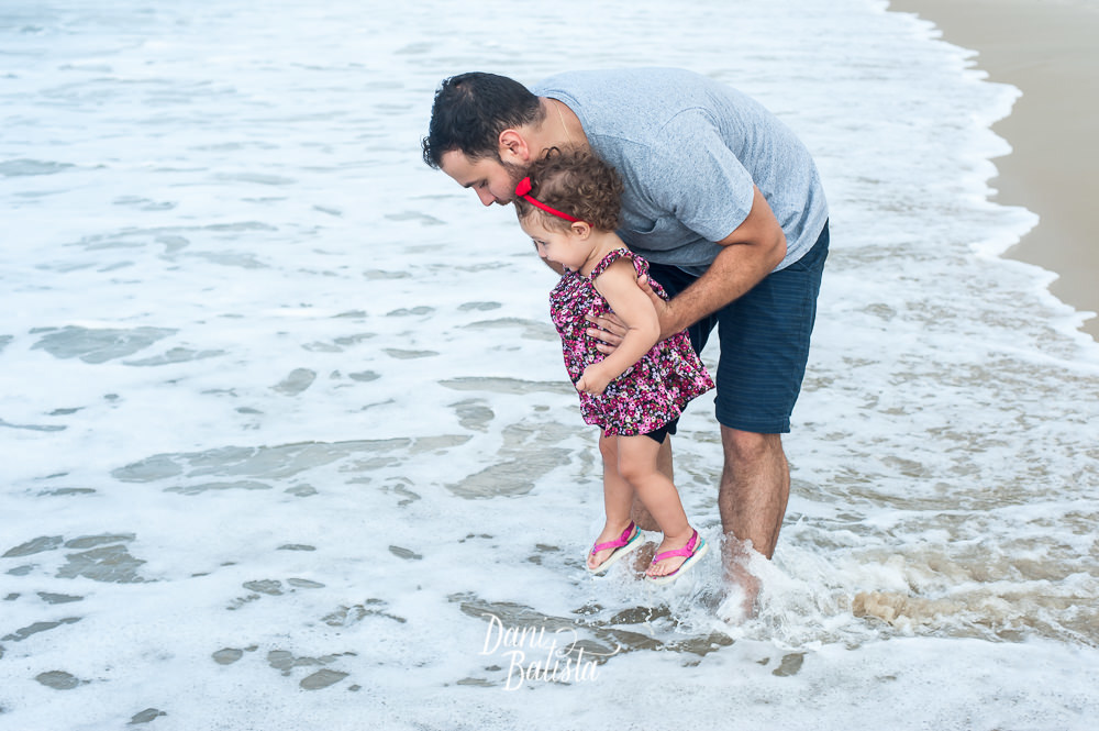 pai brincando com a filha na água da praia do leblon durante ensaio fotografico de gestante
