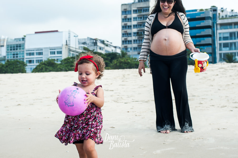 primeira filha do casal com a mãe gestante ao fundo durante ensaio fotografico na praia leblon