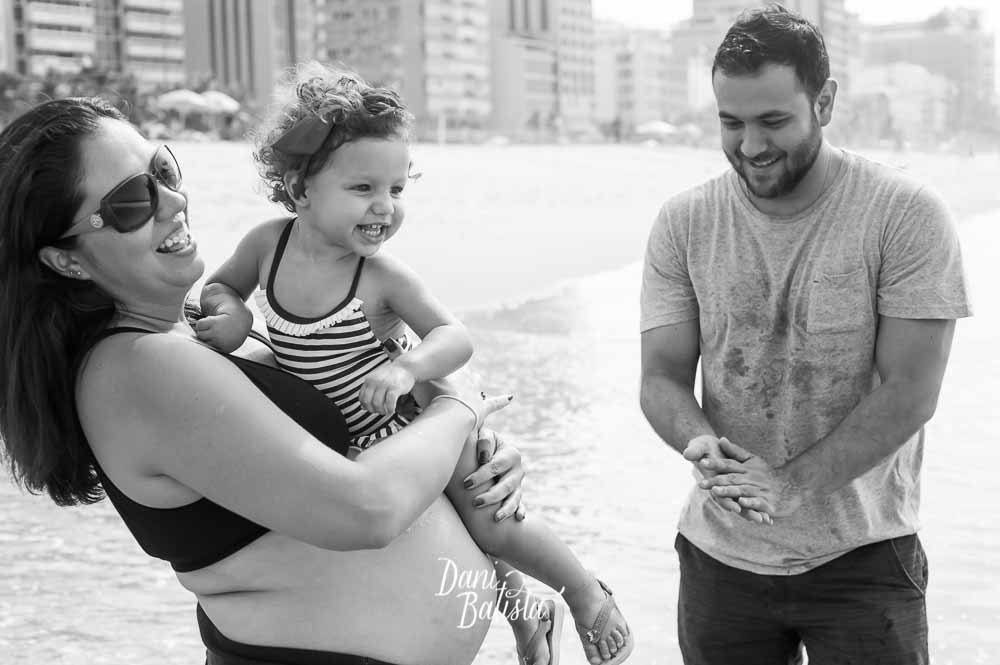 pais brincando com a primeira filha durante ensaio fotografico de gestante na praia leblon