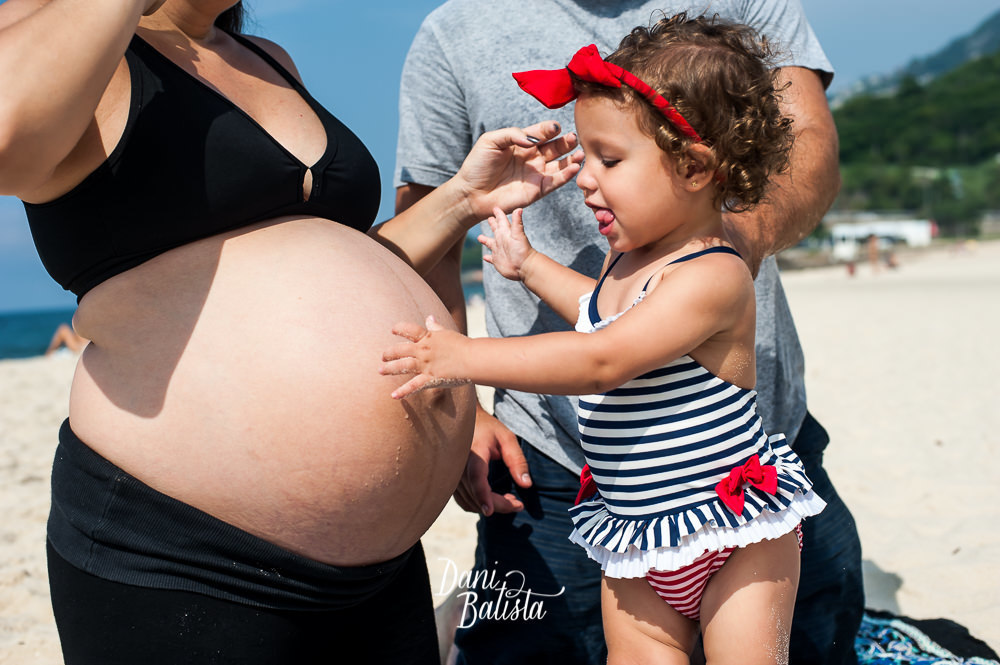 filhinha fazendo carinho na barriga da mãe durante ensaio fotografico de gestante na praia leblon
