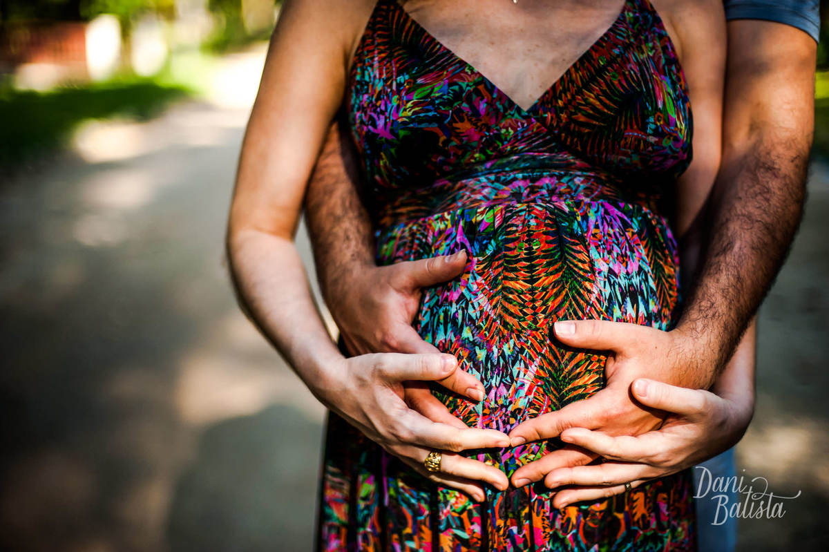 casal com mãos entrelaçadas na barriga durante ensaio fotográfico de gestante no jardim botânico do rio de janeiro