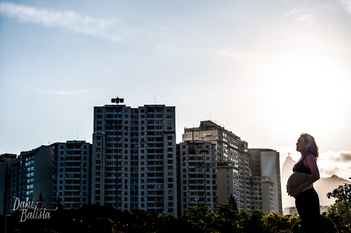 silhueta da gestante com prédios durante ensaio fotográfico no aterro do flamengo no por do sol