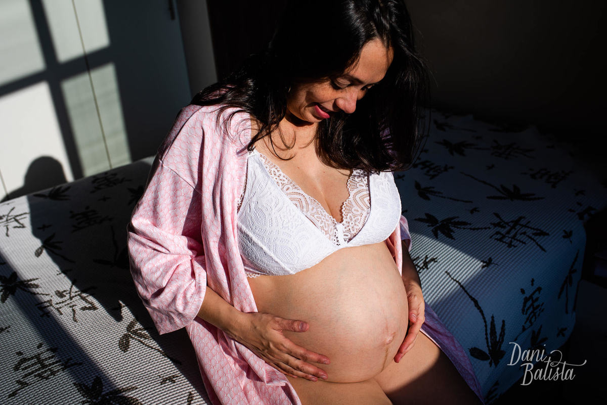 gestante fazendo carinho na barriga em cima da cama durante ensaio de Gestante em Casa