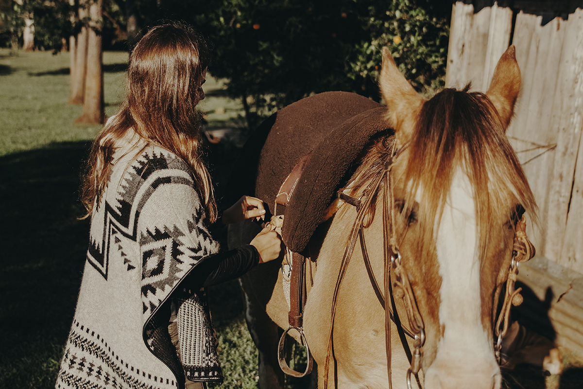 Menina arruma a cela do seu cavalo em ensaio fotográfico