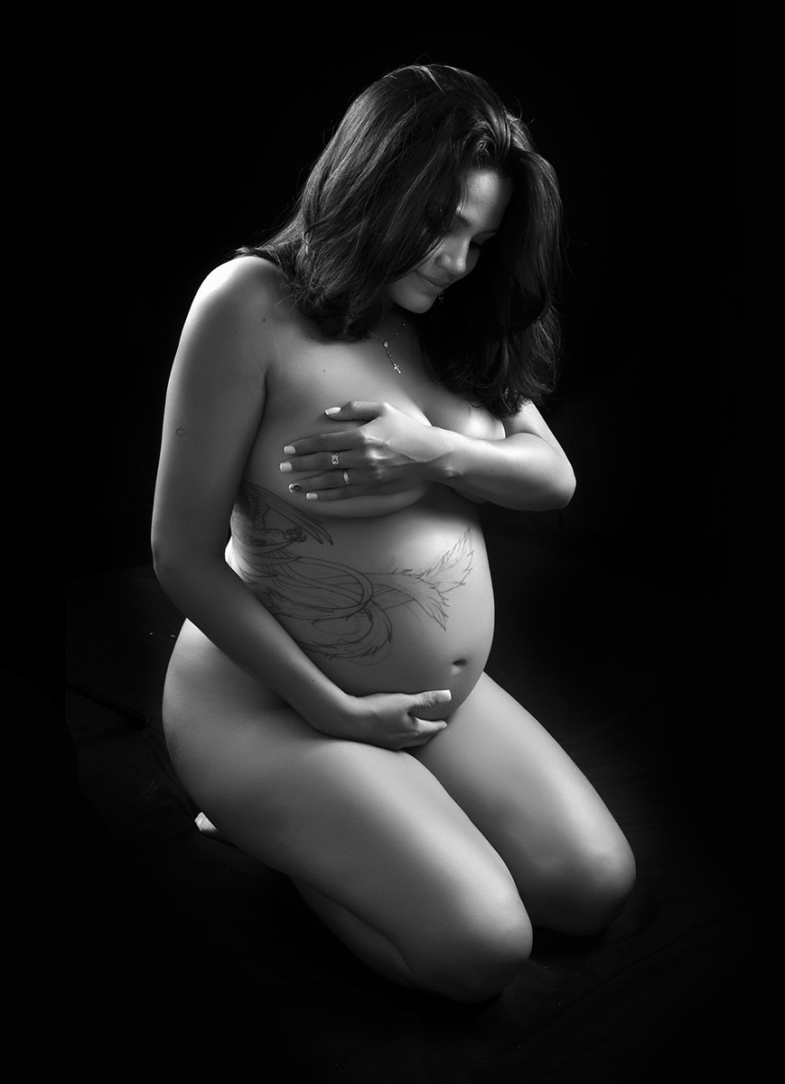 mãe sentada segurando a barriga no ensaio de gestante no estúdio  