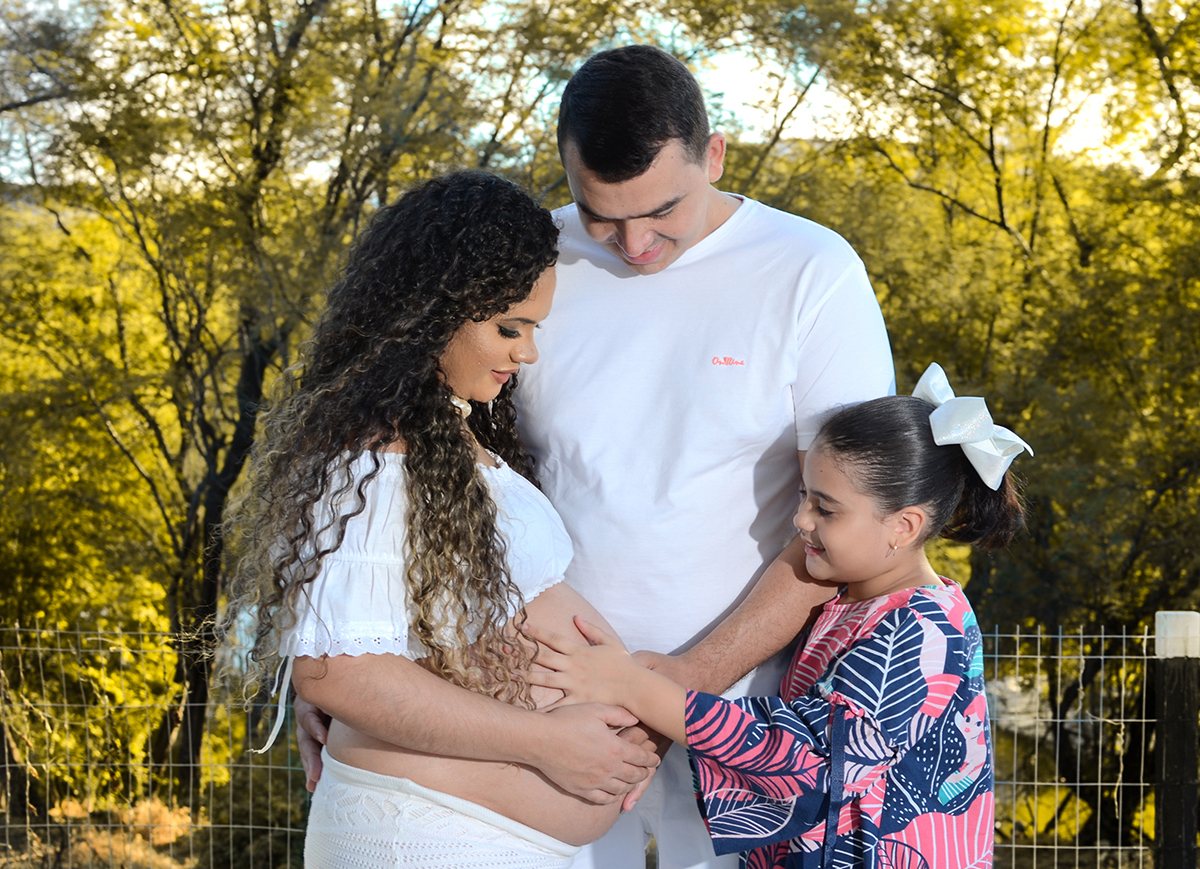 A  irmã mais velha e o pai acariciam a barriga da mãe no dia do ensaio  de gestante ao ar livre 