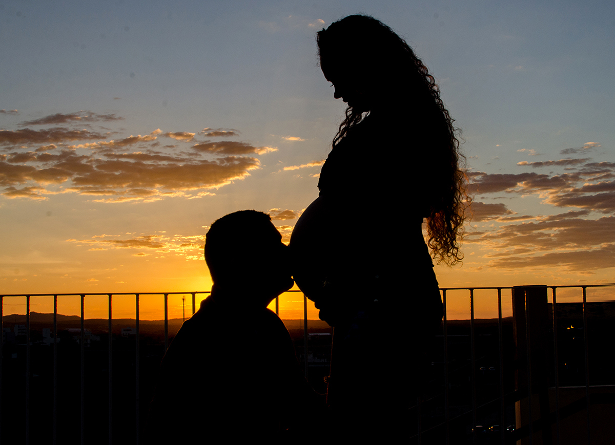 por do sol com pai beijando a barriga da mãe no dia do ensaio de gestante 