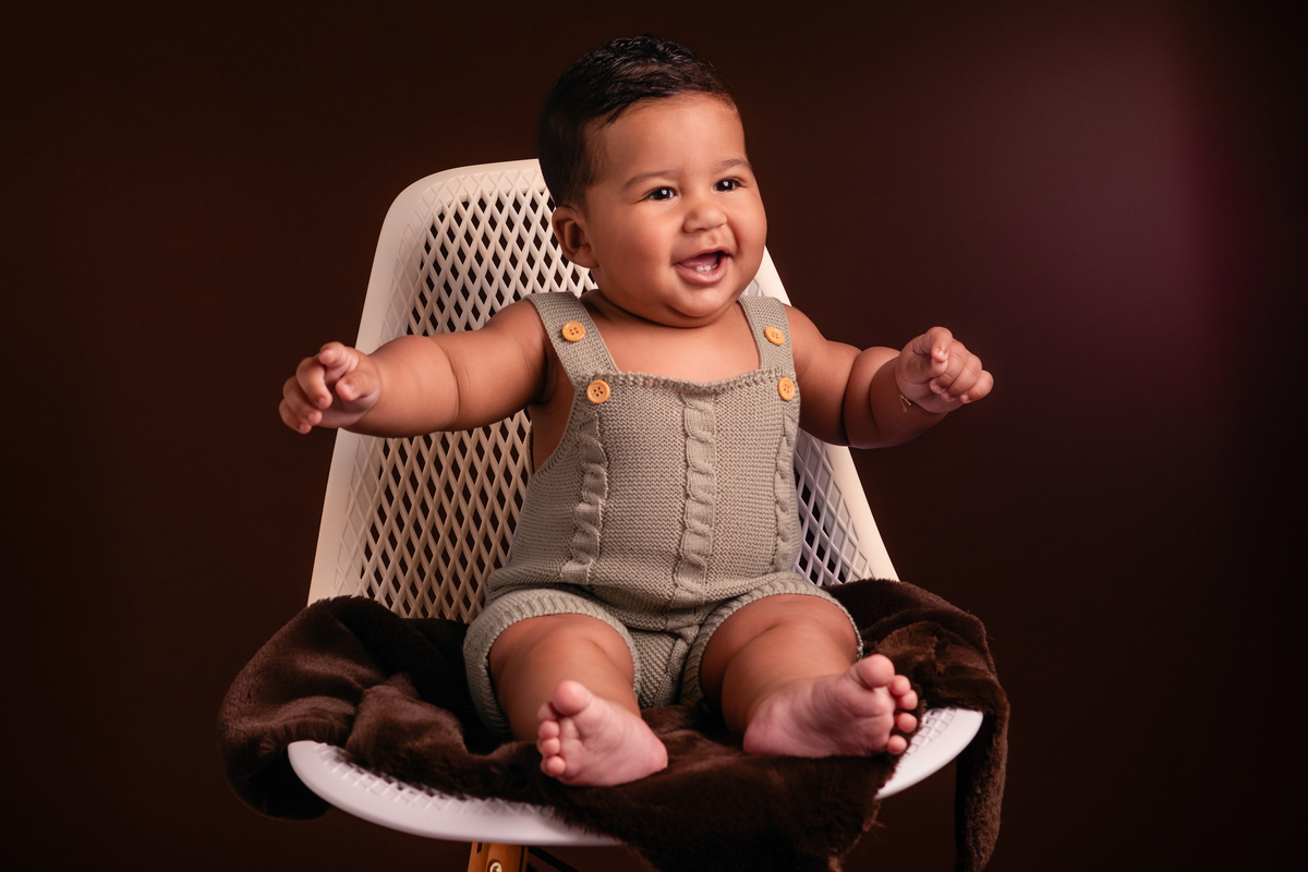 Bebê sentado na cadeira, sorrindo no seu ensaio de acompanhamento de 6 meses no Ander Lopes Fotografia em Taquara/RS