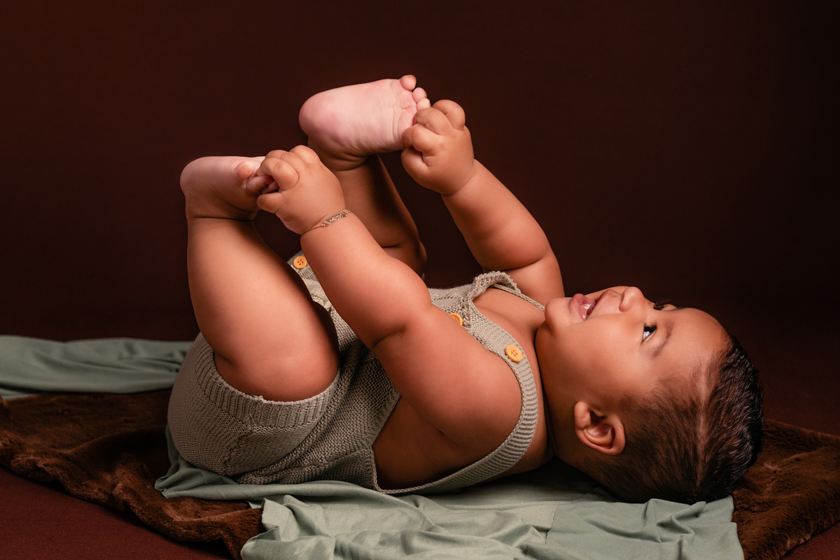 Bebê fofo deitado segurando seu pézinho, sorrindo no seu ensaio de acompanhamento de 6 meses no Ander Lopes Fotografia em Taquara/RS