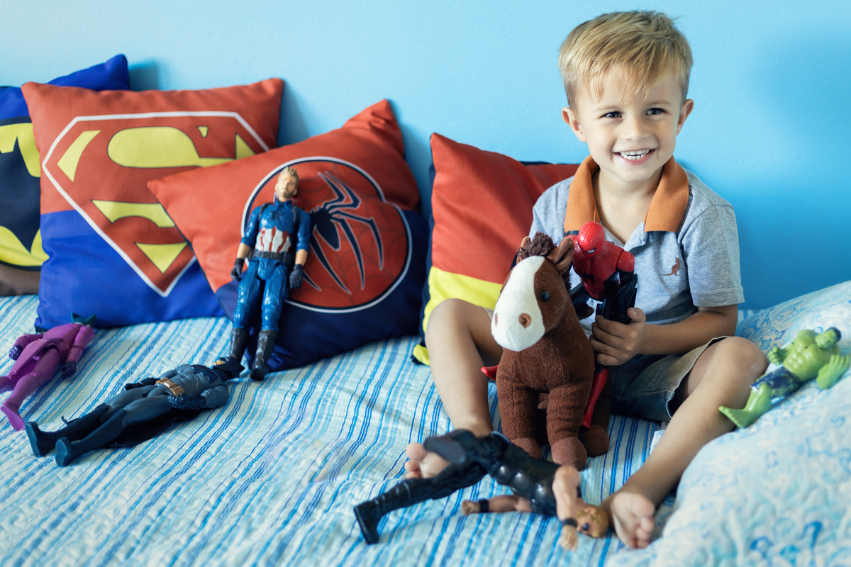 Ensaio infantil de menino na cama com brinquedos e super herois