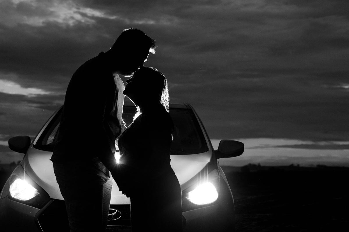 Foto de gestante com o pai e na frente do carro com farol ligado