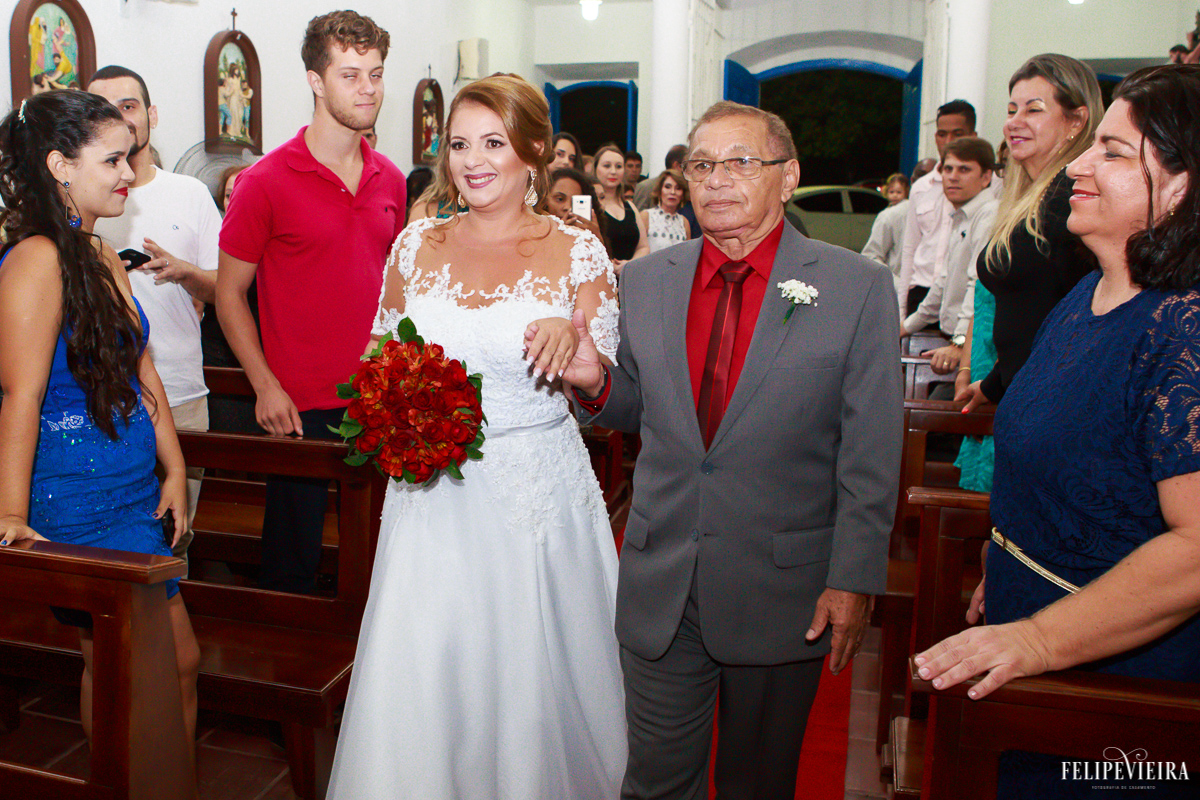 Noiva com um belo sorriso entrando na igreja com seu pai segurando um buquê vermelho fotografia de casamento em Guarapari-ES Felipe Vieira.