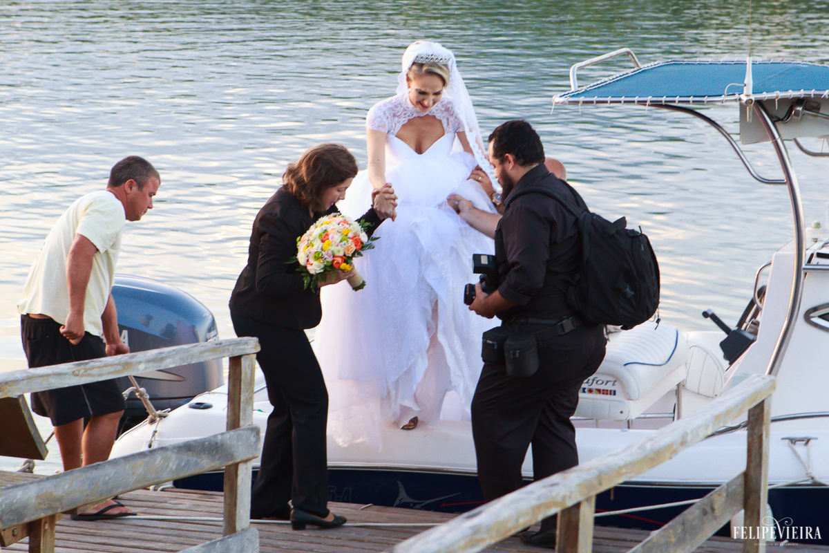 fotógrafo felipe vieira e cerimonialista ajudando a noiva a descer da lancha no casamento à beira do mar foto da fotógrafa jany tesch vieira fotografia de casamento em Guarapari