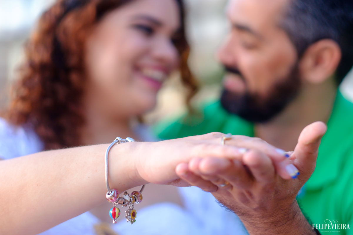 marido e esposa de mãos dadas com detalhe da pulseira dela onde tem pingentes de crianças foto feita por felipe vieira fotógrafo de gestantes