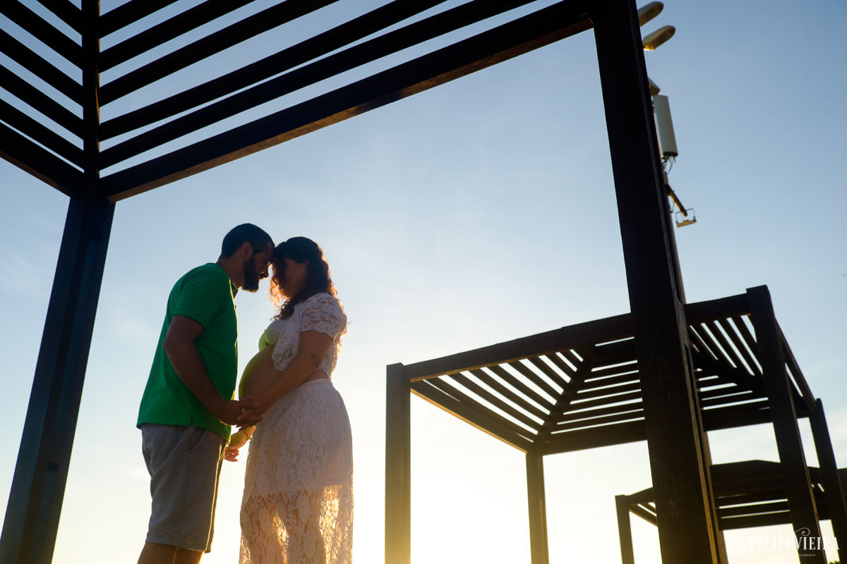casal feliz de mãos dadas à espera de seu futuro filho com um belo céu azul no fundo foto feita por felipe vieira fotógrafo de gestantes