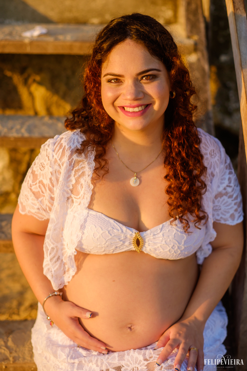 gestante sorrindo feliz com a luz do pôr do sol na praia do morro guarapari foto feita por felipe vieira fotógrafo de gestantes