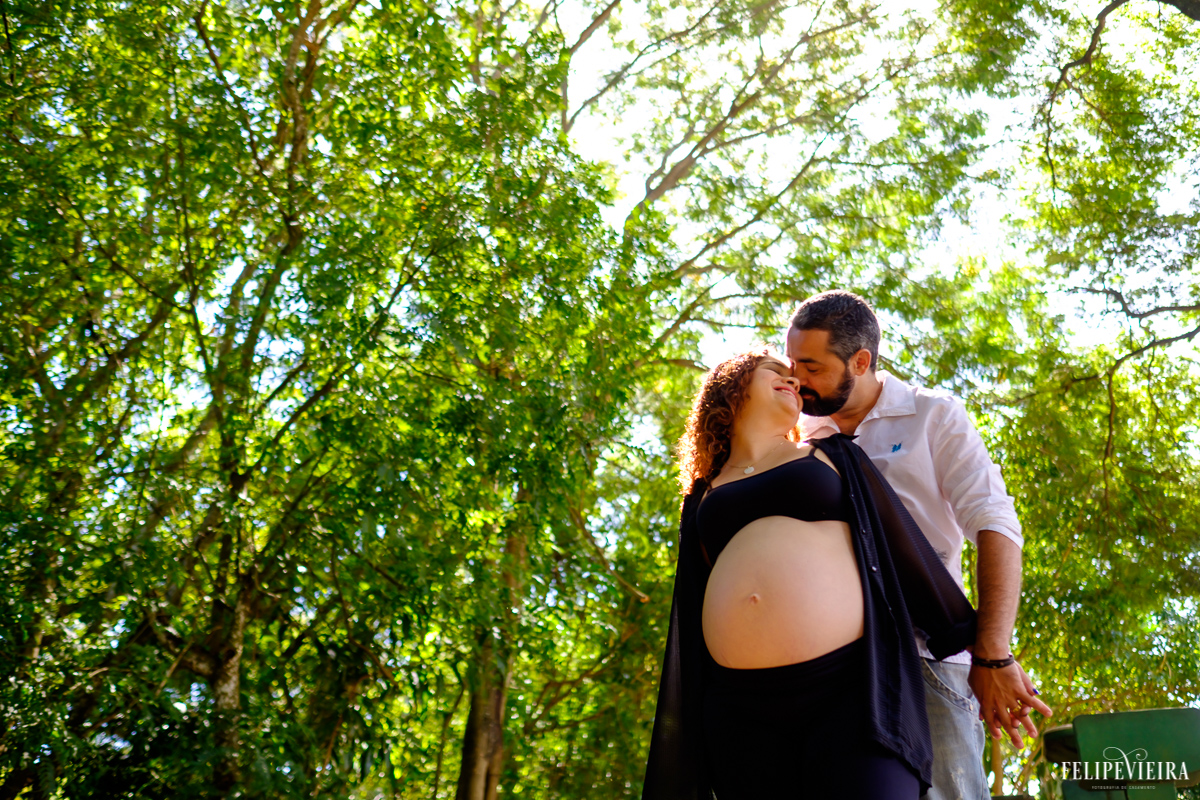 futuros pais abraçados e felizes com um fundo verde e a barriga da gestante bem destacada foto feita por felipe vieira fotógrafo de gestantes