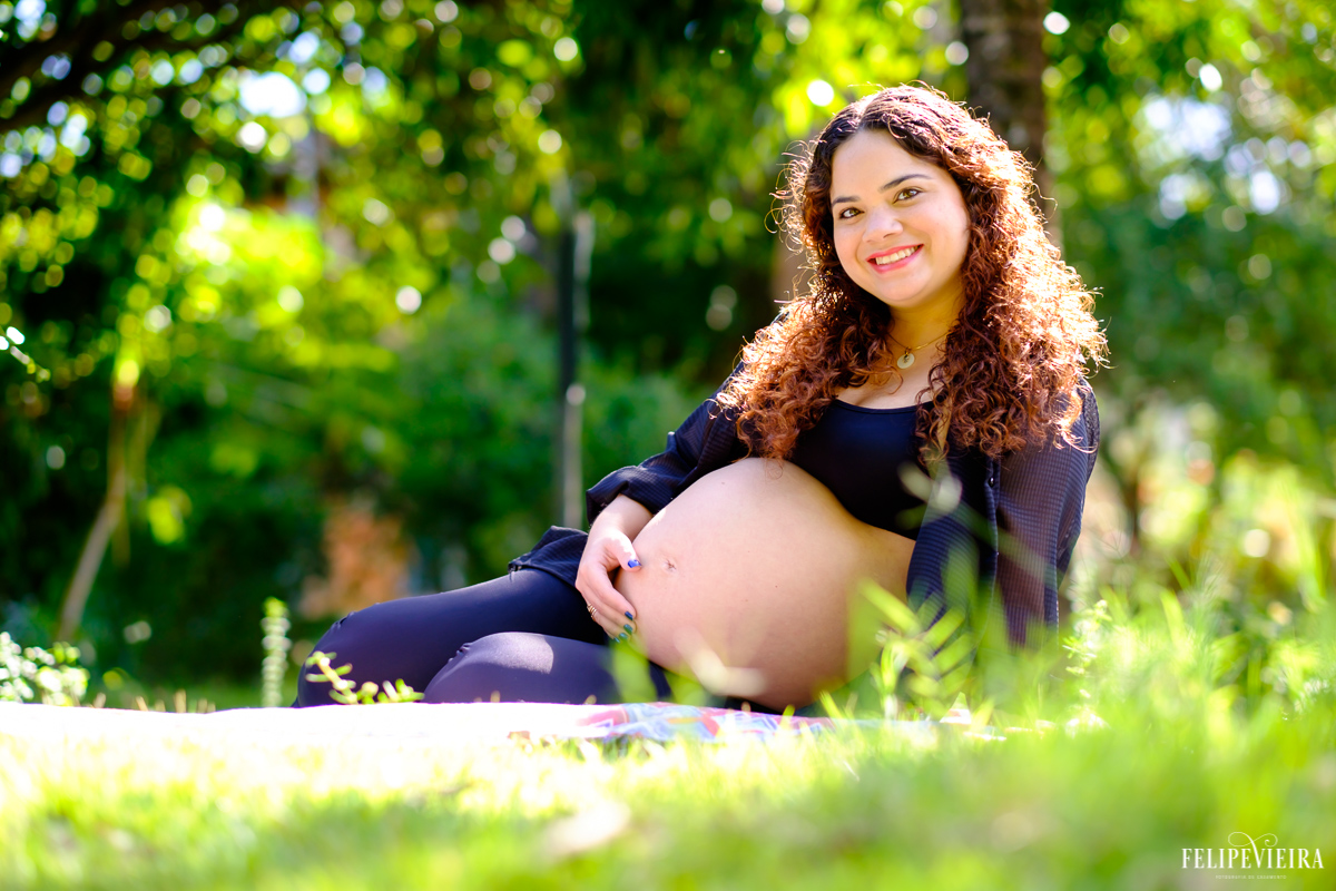 gestante deitada na grama e sorrindo com a mão na barriga foto feita por felipe vieira fotógrafo de gestantes