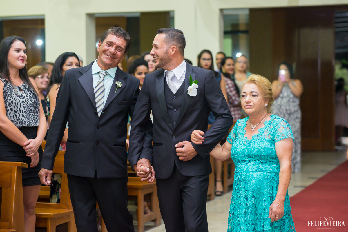 noivo entrando com seus pais na igreja e sorrindo bastante foto feita por Felipe Vieira fotógrafo de casamentos em Guarapari