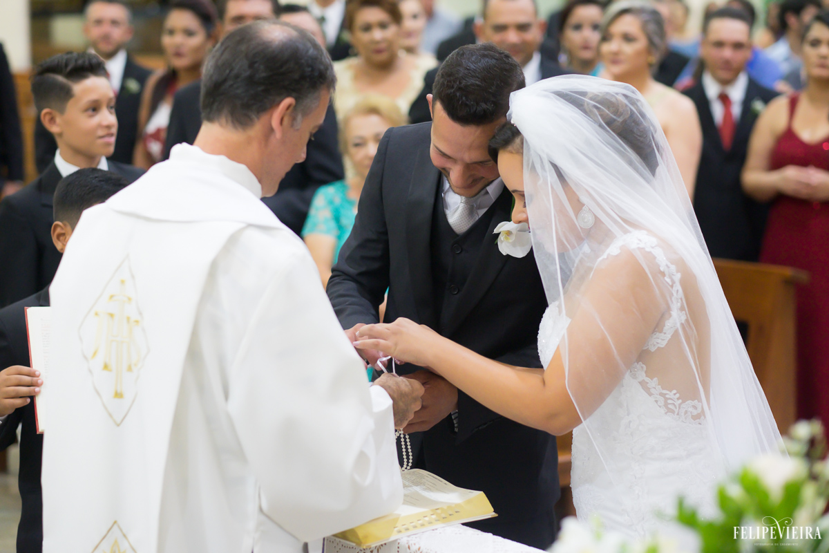 Noivos pegando suas alianças nas mãos do padre sorrindo foto feita por Felipe Vieira fotógrafo de casamentos em Guarapari