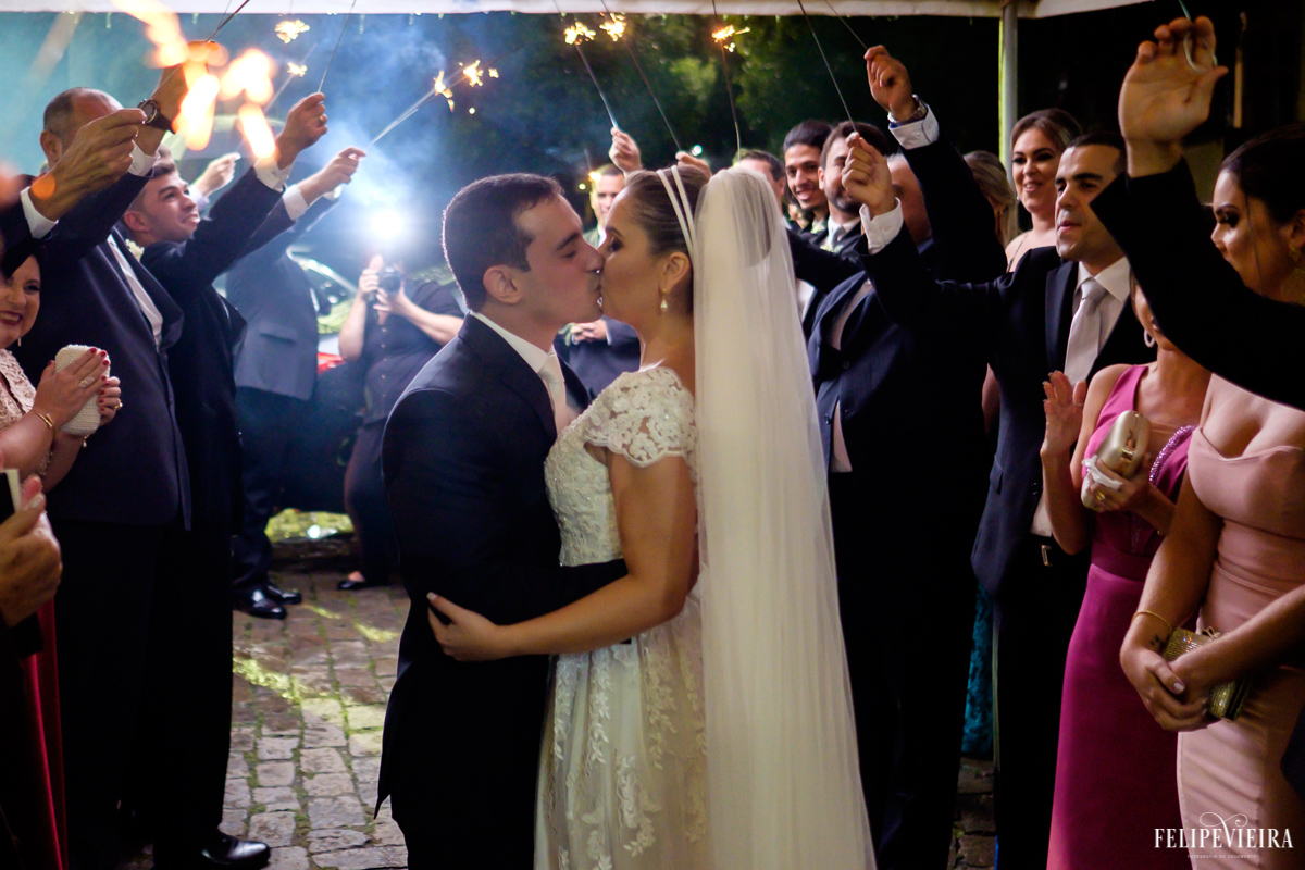 beijo do casal na saída da igreja com todos os padrinhos os recebendo foto feita por Felipe Vieira fotógrafo de casamentos em Guarapari