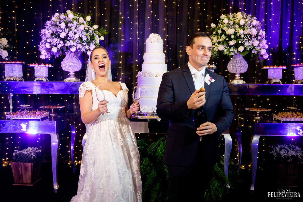 noivos rindo alegres após o estouro do champanhe na mesa do bolo foto feita por Felipe Vieira fotógrafo de casamentos em Guarapari
