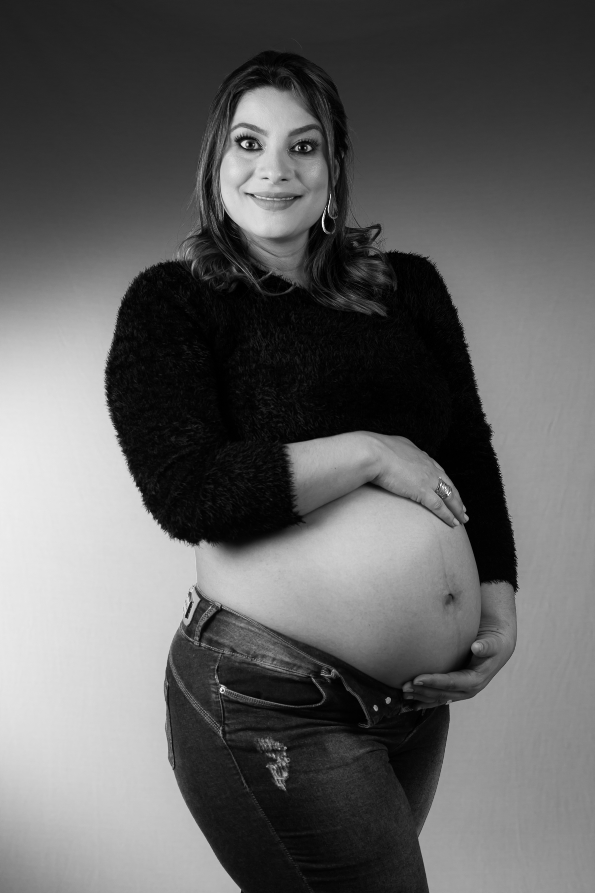 Ensaio de gestante em estúdio com roupas de seda e luz natural. Fotografia de grávida com expressão serena e suave.
