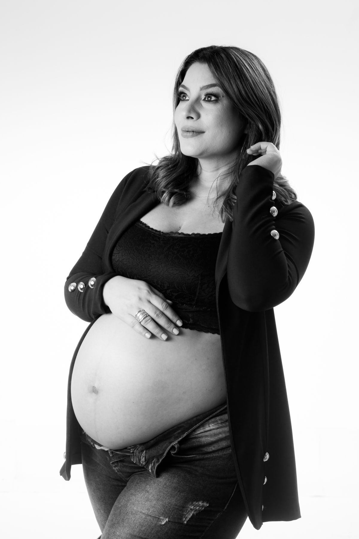 Sessão de fotos de grávida em estúdio com fundo branco e luz suave. Ensaio de gestante com roupas discretas e postura relaxada.