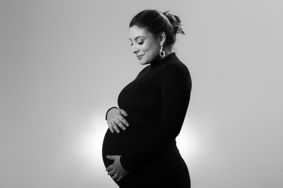 Ensaio de gestante em estúdio com luz de fundo e roupas delicadas. Fotografia de grávida com expressão natural e suave.
