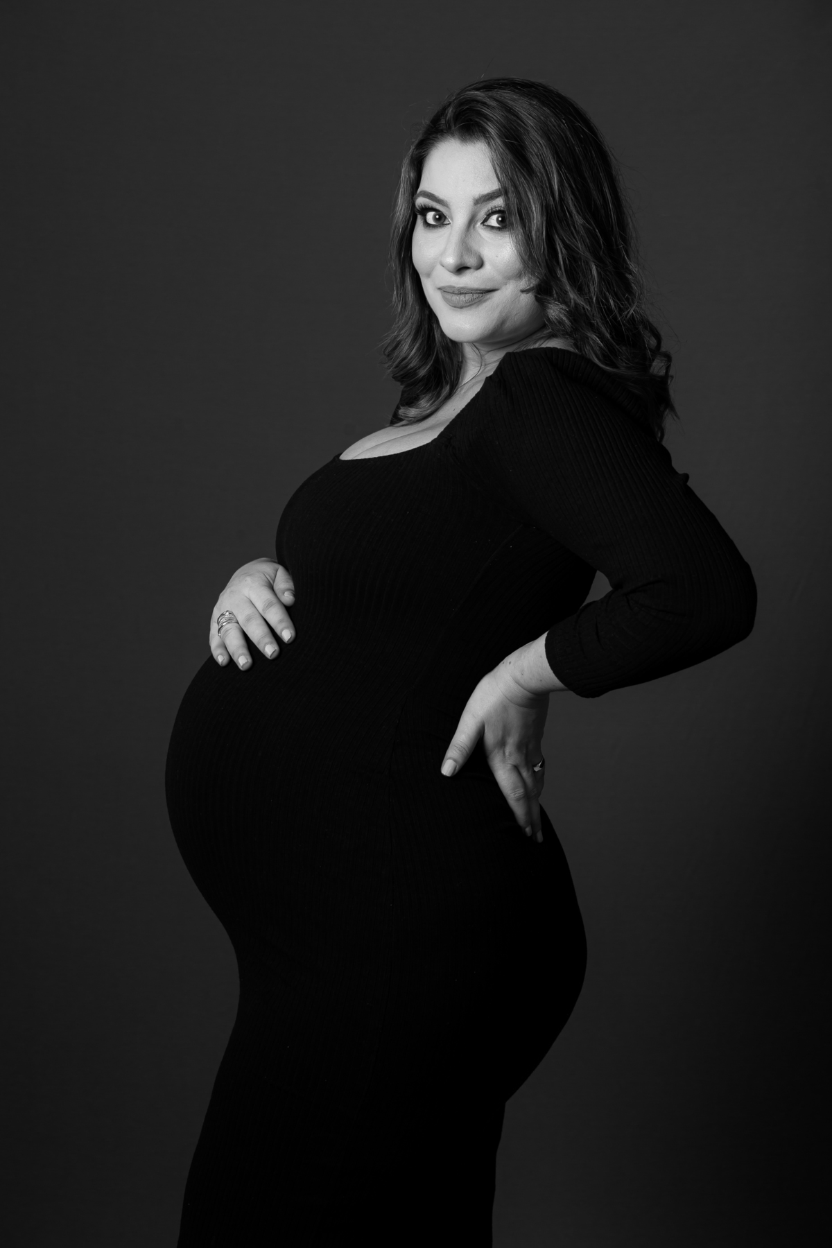 Fotografia de gestante com iluminação suave e ambiente intimista. Ensaio de grávida com foco na barriga e nas mãos.