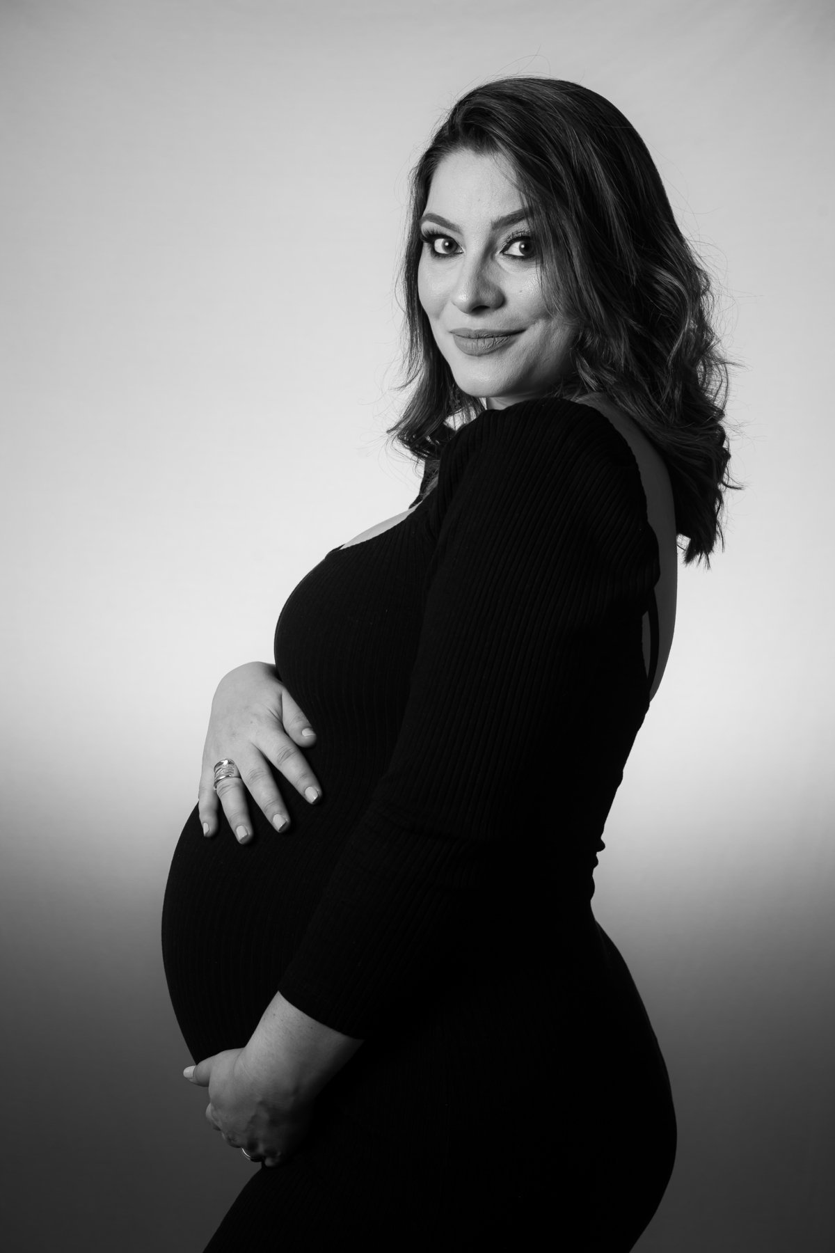 Book de gestante com fundo neutro e luz suave no estúdio. Sessão de fotos de grávida com roupa clássica e feminina.