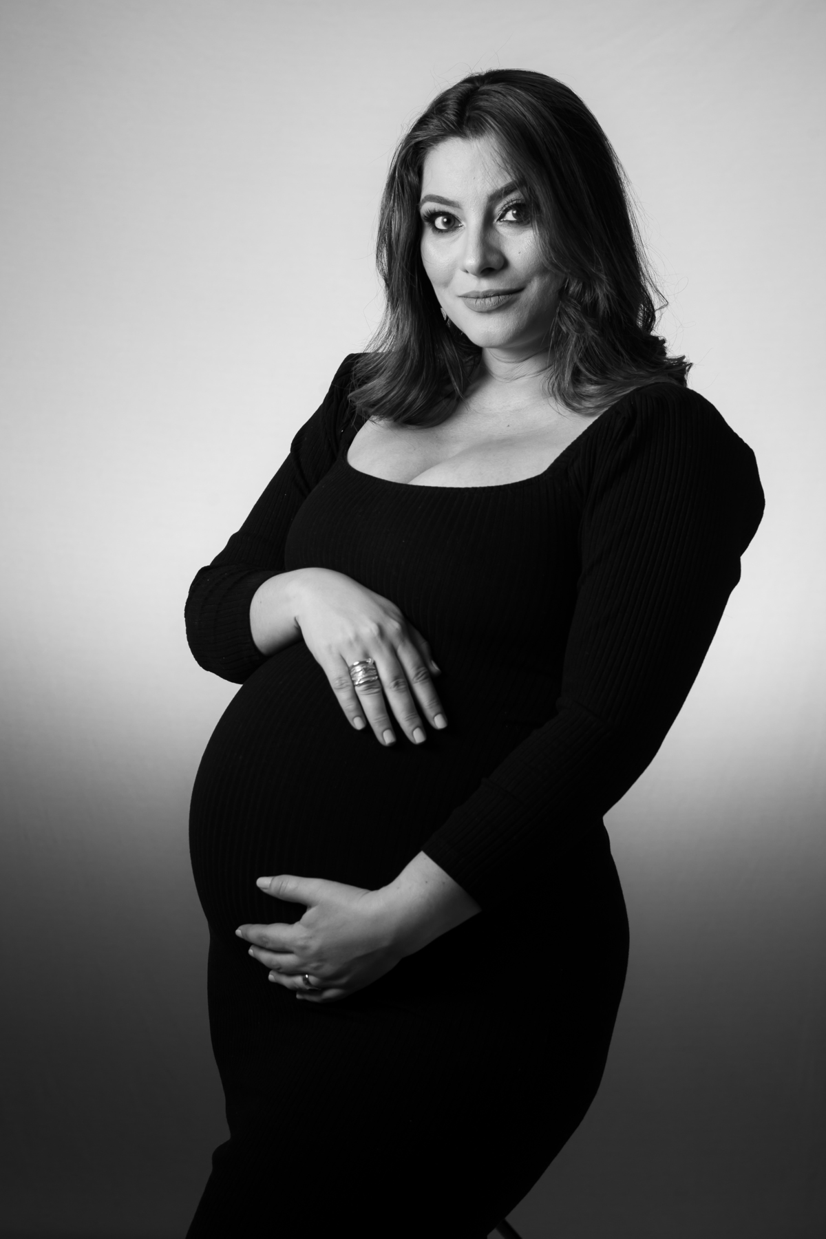 Book de gestante em estúdio com iluminação suave e natural. Sessão de fotos de grávida com foco no rosto e nas mãos.