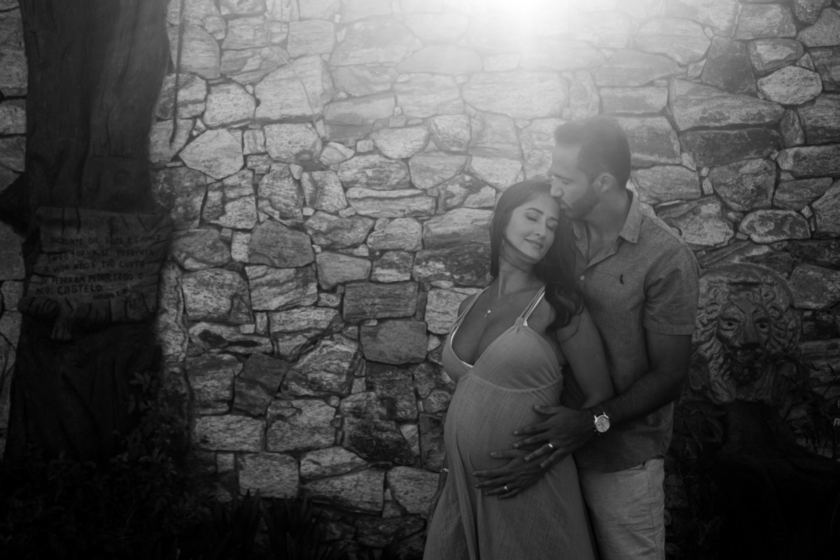 Fotograia de gestante com o marido em frente a um muro de pedras. Fotografia em preto e branco 