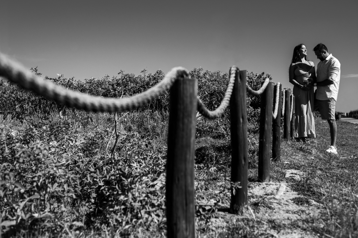 Book de gestante com clima romântico à beira-mar. Ensaio de gestante com marido na praia ao pôr do sol. Fotografia em preto  branco