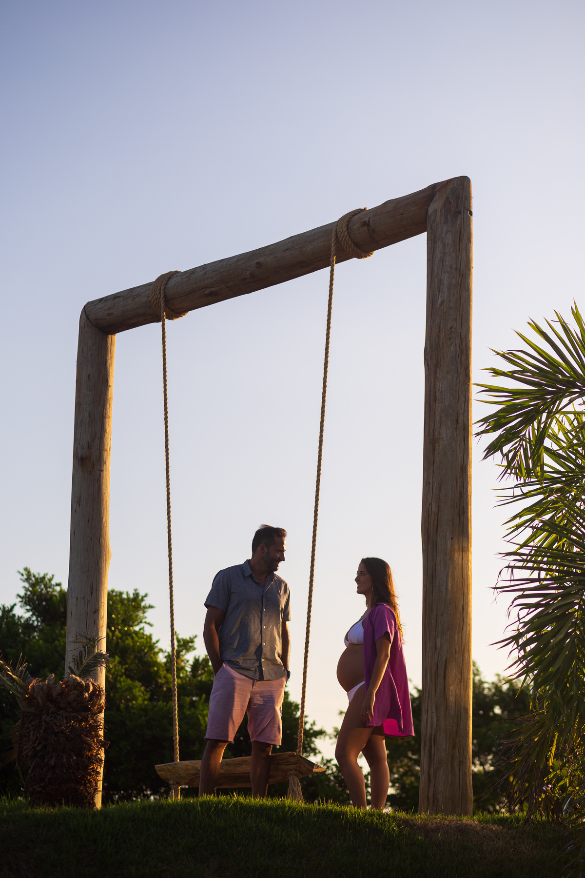 Ensaio de gestante com marido à beira-mar ao entardecer. Fotografia de gravidez com sombras e luz natural da praia.