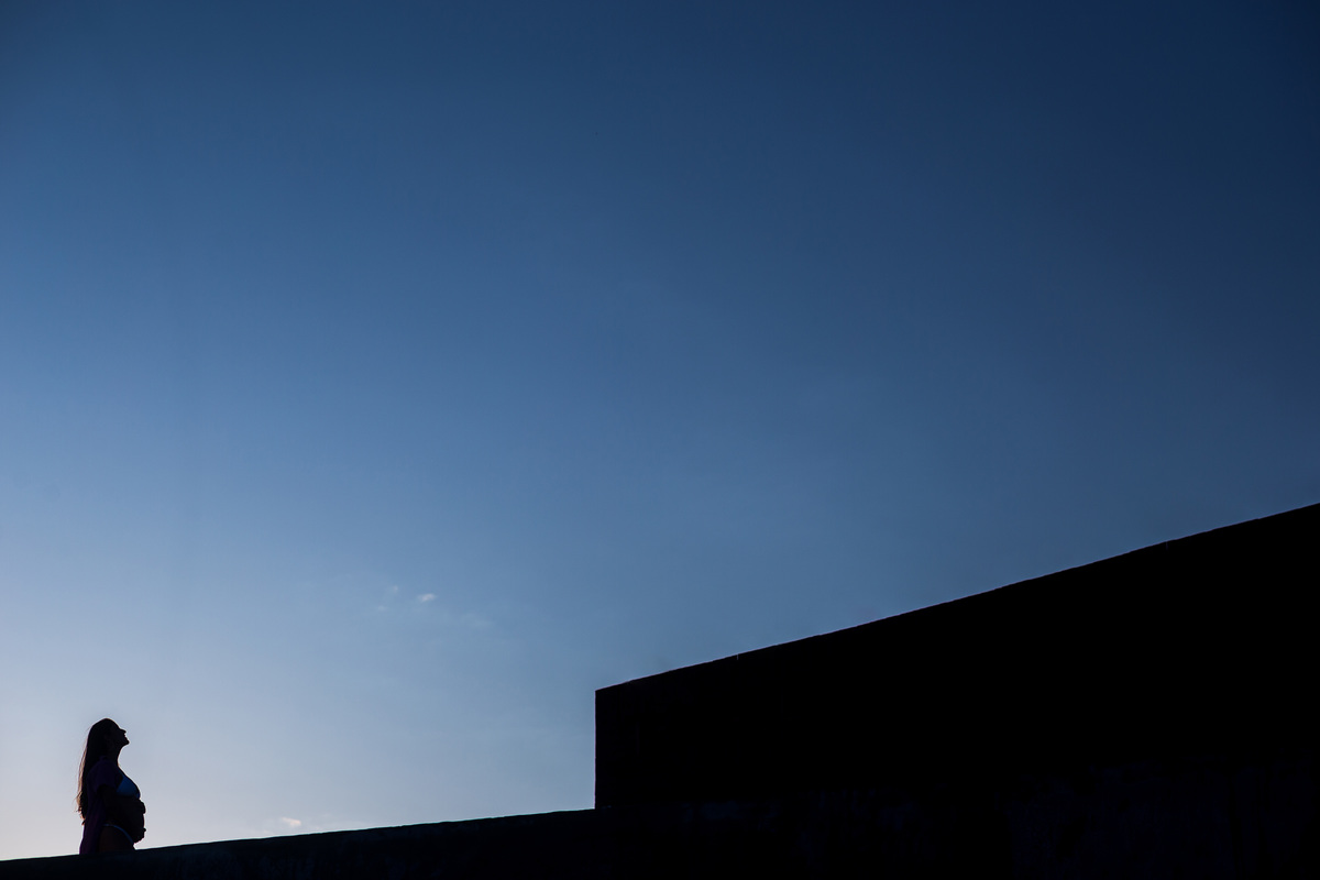 Fotografia de gestante com detalhes de natureza à beira-mar. Ensaio fotográfico de grávida em praia com céu azul. SIlhueta da gestante contra o céu azul
