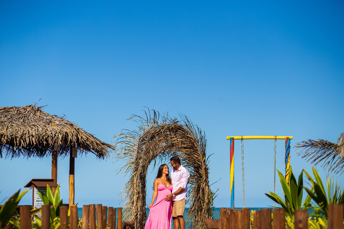 Book de gestante com atmosfera romântica à beira-mar. Fotografia de gravidez com vestido leve na praia numa bela tarde de céu azul
