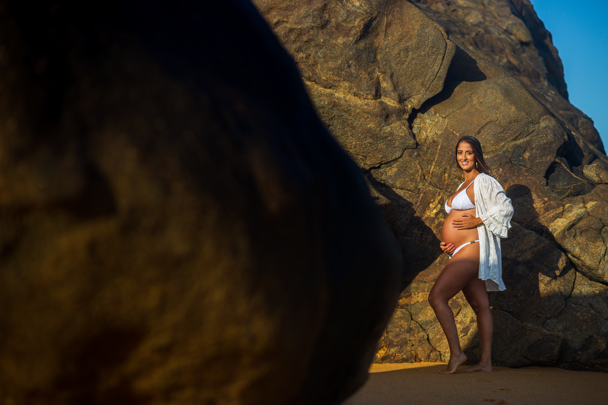 Book gestante em praia paradisíaca com céu azul e mar tranquilo. Fotografia de gestante com elementos naturais da praia.