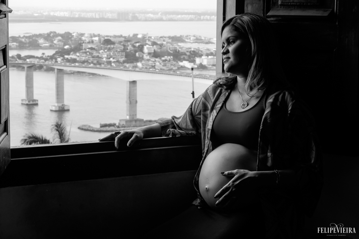 gestante sentada na beira da janela com a terceira ponte de vitória ao fundo foto feita por felipe vieira fotógrafo de gestantes