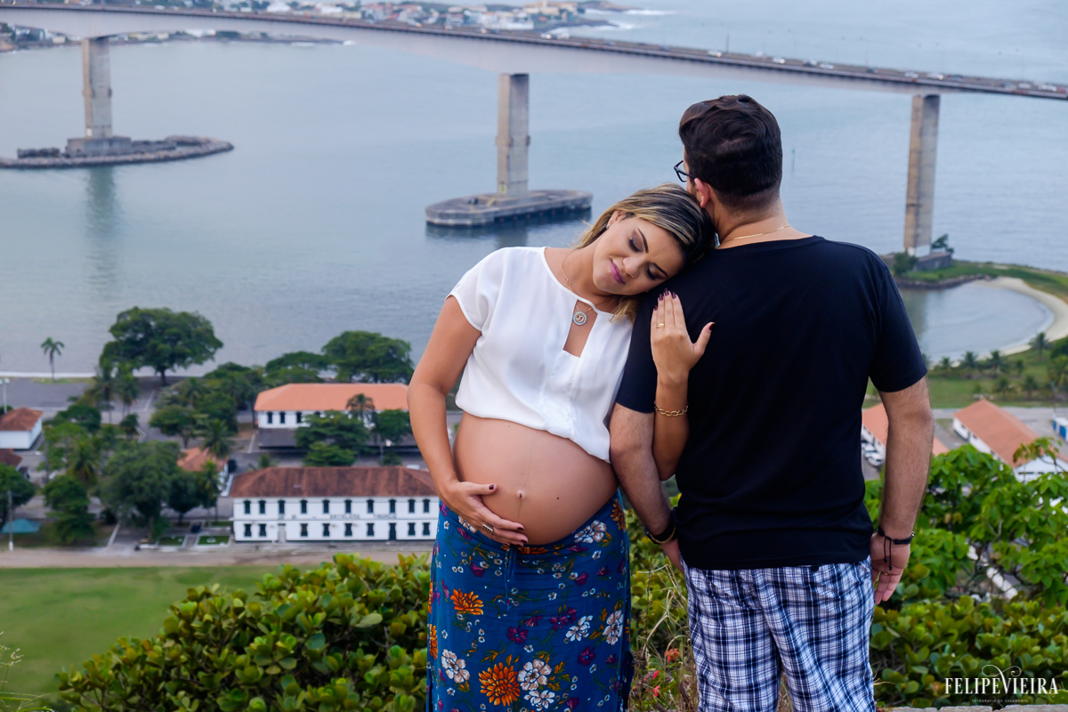 foto de família onde a gestante e seu marido posam abraçados e com a terceira ponte de vitória ao fundo