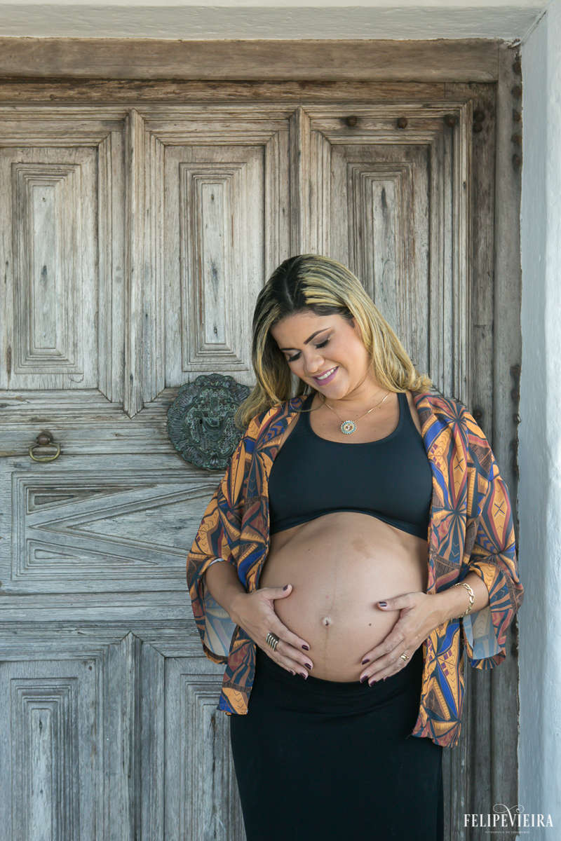 gestante feliz ao olhar para barriga com as mãos nela em frente a porta do convento foto feita por felipe vieira fotógrafo de gestantes