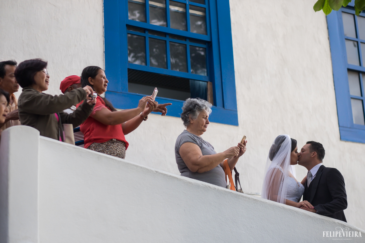 Noivos se beijando enquanto pessoas a sua volta tiram fotos do momento foto feita por felipe vieira fotógrafo de casamentos no convento da penha